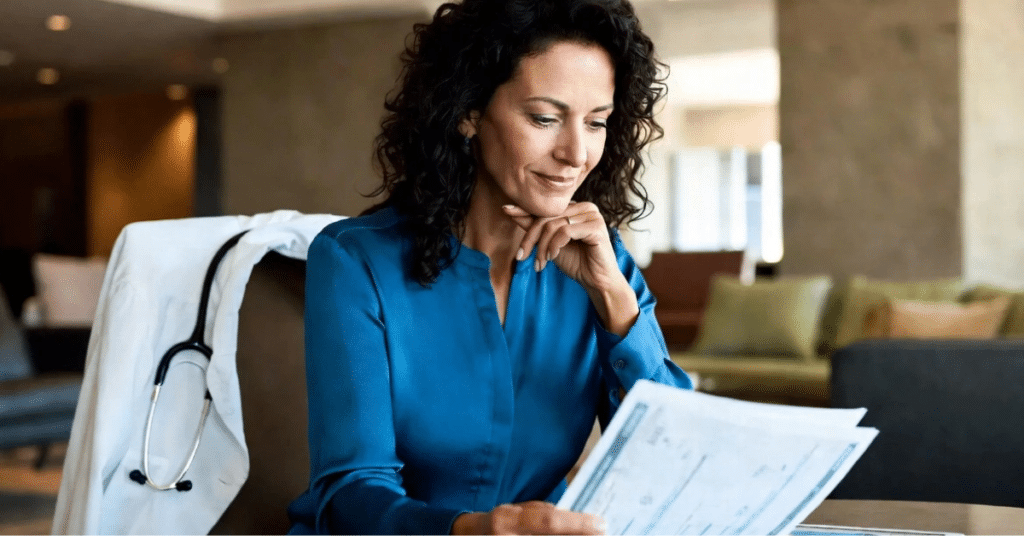 red-flags-syndication-due-diligence-checklist.webp Female physician in a professional setting reviewing investment documents, with a white coat and stethoscope visible, representing a high-income accredited investor evaluating alternative investments