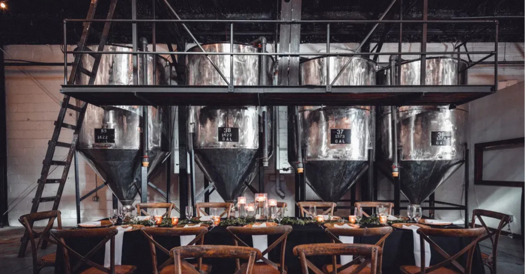 Winemaker_Hall_tanks_Renault_Winery_Resort Elegant event table set inside Winemaker Hall at Renault Winery Resort in Egg Harbor City, New Jersey, with historic fermentation tanks as a backdrop and string lights overhead